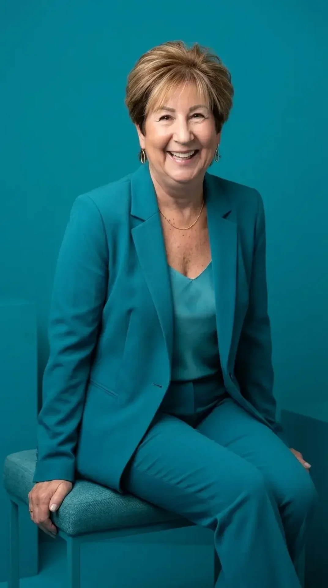 AI brand portrait of Ellen in a teal suit seated on a tonal set